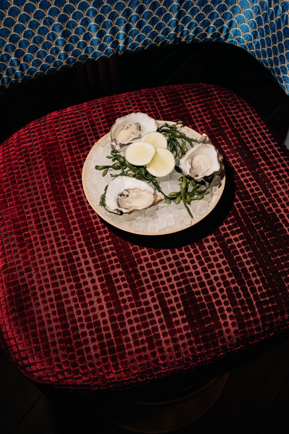 Verse oesters op ijs met limoenpartjes, geserveerd op een rood fluwelen stoel