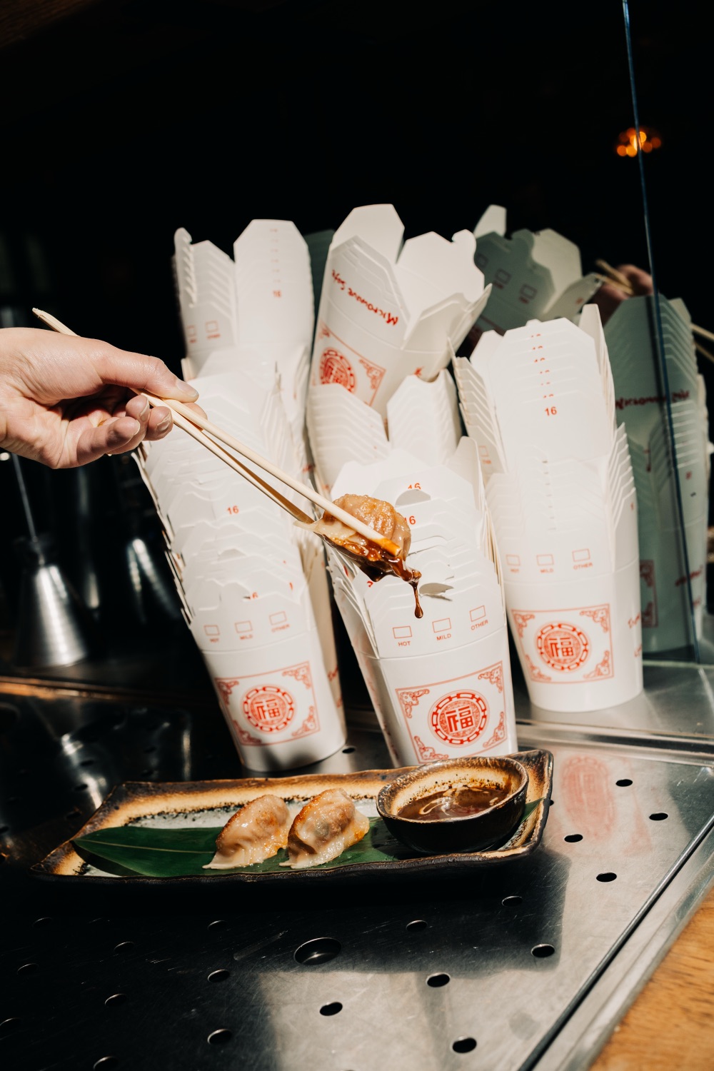 Stokjes tillen een dumpling op die druipt van de saus, met takeout-bakjes op de achtergrond
