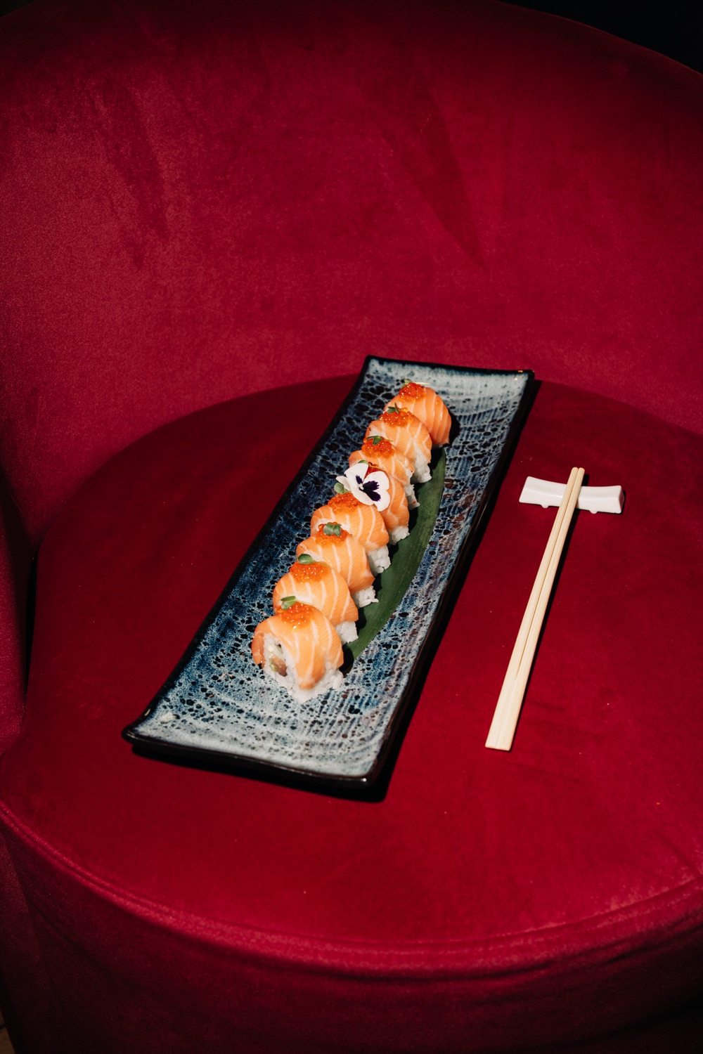 Salmon sushi rolls on a blue platter placed on a red velvet chair
