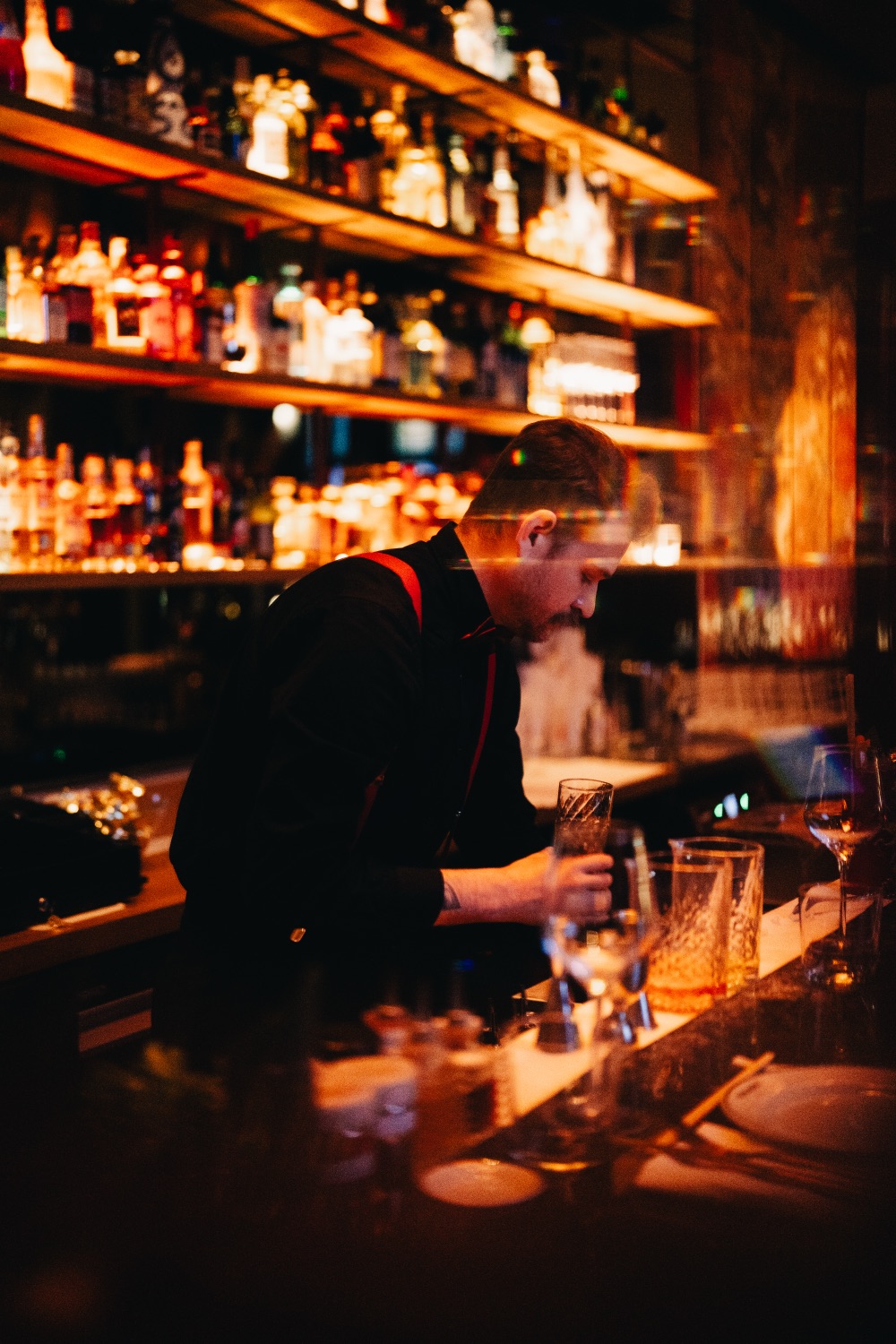 Bartender maakt een cocktail achter een sfeervol verlichte bar met flessen op de planken