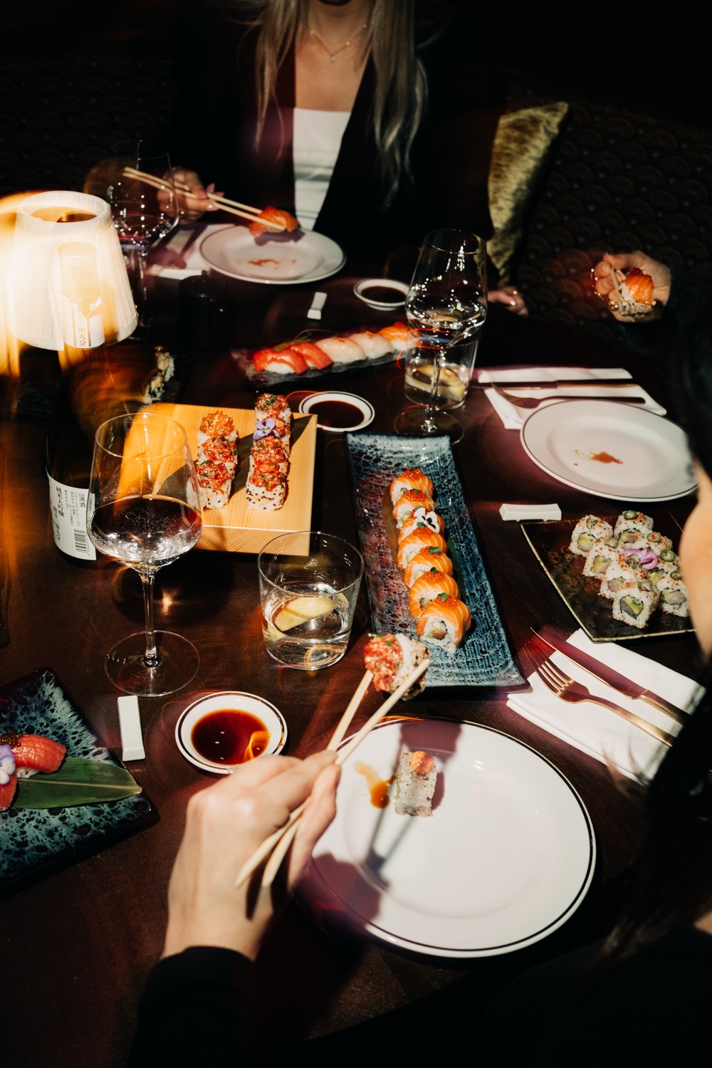 Vrienden delen sushi en wijn aan een sfeervol verlichte restauranttafel
