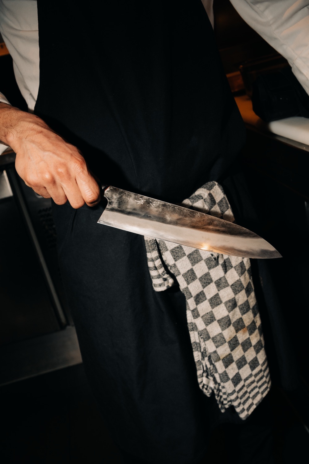 Close-up van een chef in een zwart schort met een groot keukenmes