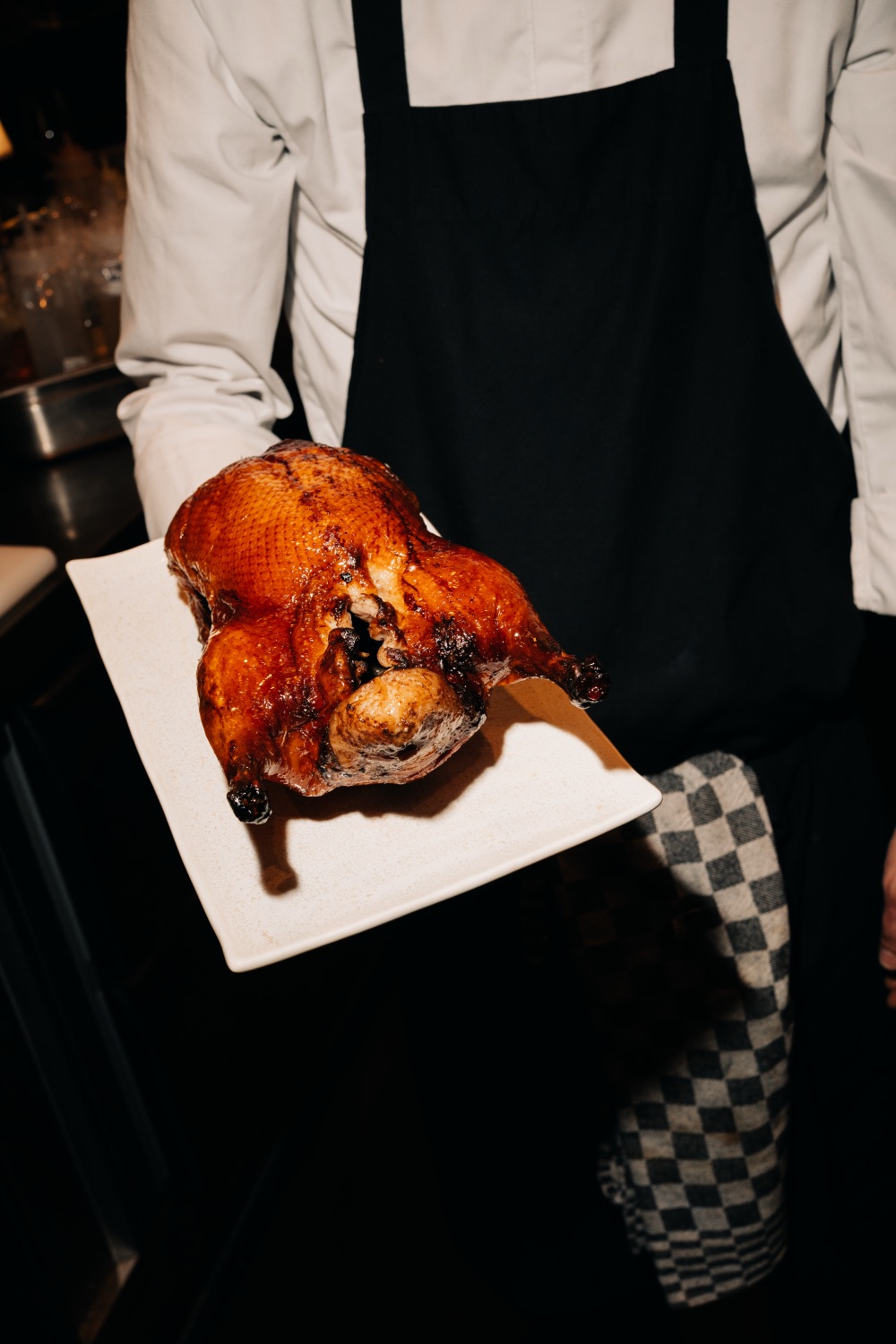 Chef holding a whole roasted Peking duck on a white serving platter
