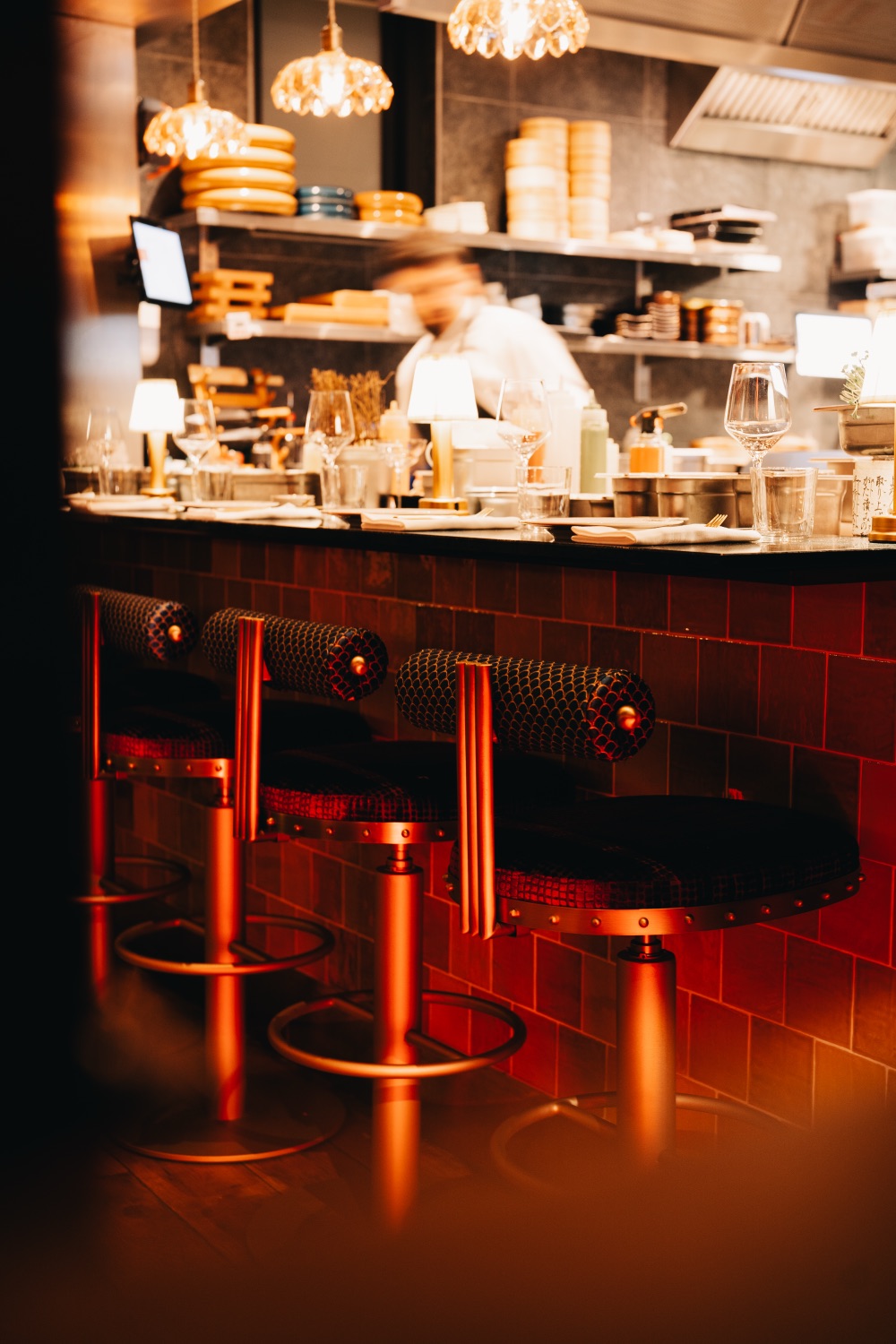 Warm verlichte bar met krukken en een chef die op de achtergrond werkt
