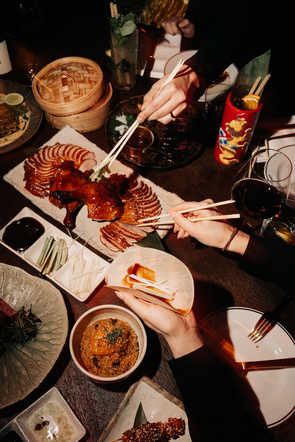 Hands reaching across a shared table of robata skewers and small plates